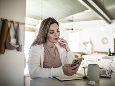 A woman sits at a kitchen counter looking at a smartphone